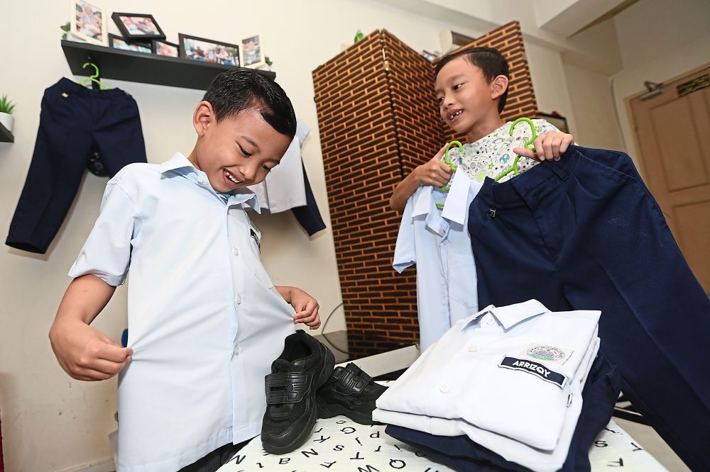 Handed down: Seven-year-old Arruzain Izzul (left) received his brother’s Arriqqy Izzran old school uniforms at their home in Shah Alam. — IZZRAFIQ ALIAS/The Star