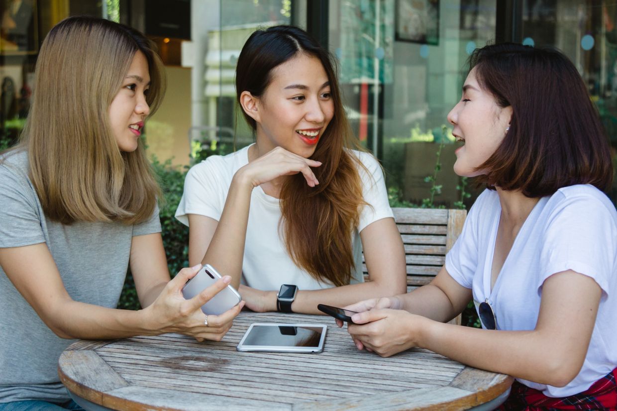 Cheerful asian young women sitting in cafe drinking coffee with friends and talking together. Attractive asian woman enjoying coffee while using smartphone for talking, reading and texting.