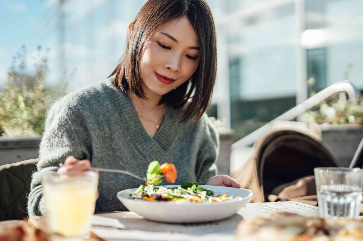Beautiful young Asian woman eating vegetable salad at a vegan cafe in a sunny afternoon. Healthy eating and lifestyles.