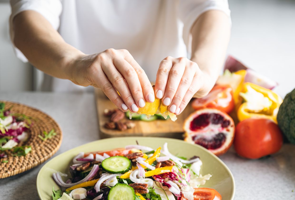 A woman makes a salad of fresh vegetables, squeezes the juice of a lemon, close-up, the concept of diet and healthy eating.