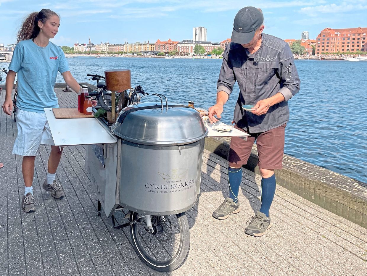Danish chef Morten Kryger Wulff cooks on his self-designed kitchen-bike during a stop of agastronomical bike tour on July 2, 2025 in Copenhagen, Denmark. With a long-standing passion for the outdoors, Danish chef Morten Kryger Wulff takes his customers on gastronomical bike ride through the Danish capital. (Photo by Camille BAS-WOHLERT / AFP)