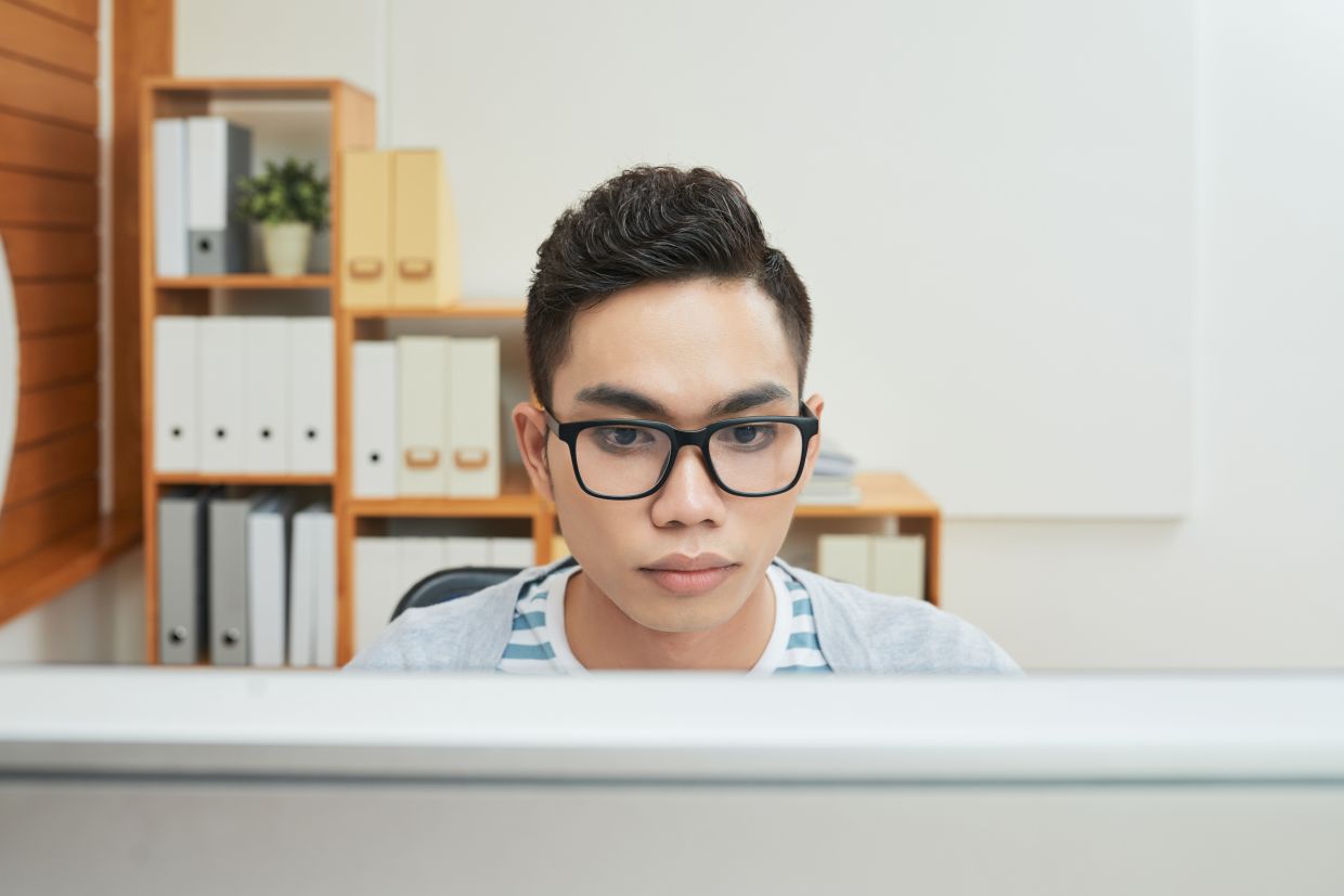 Modern Asian man in glasses focused on computer while working in office