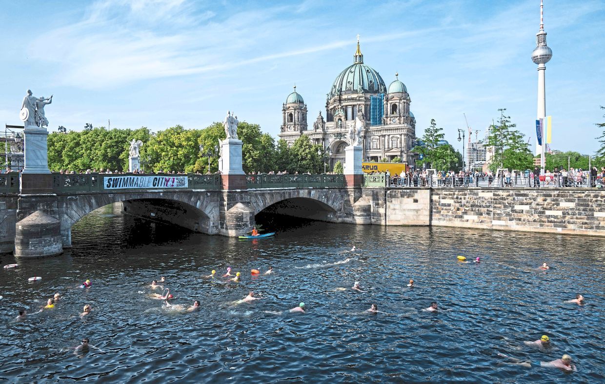 Swimmers bathe in the Spree canal in front of the Berlin Cathedral (Berliner Dom) and the TV Tower during a demonstration to mark the 100th anniversary of a ban on swimming in the Spree river, in Berlin on June 17, 2025. The demonstrators are pleading for a lifting of the ban. (Photo by John MACDOUGALL / AFP)