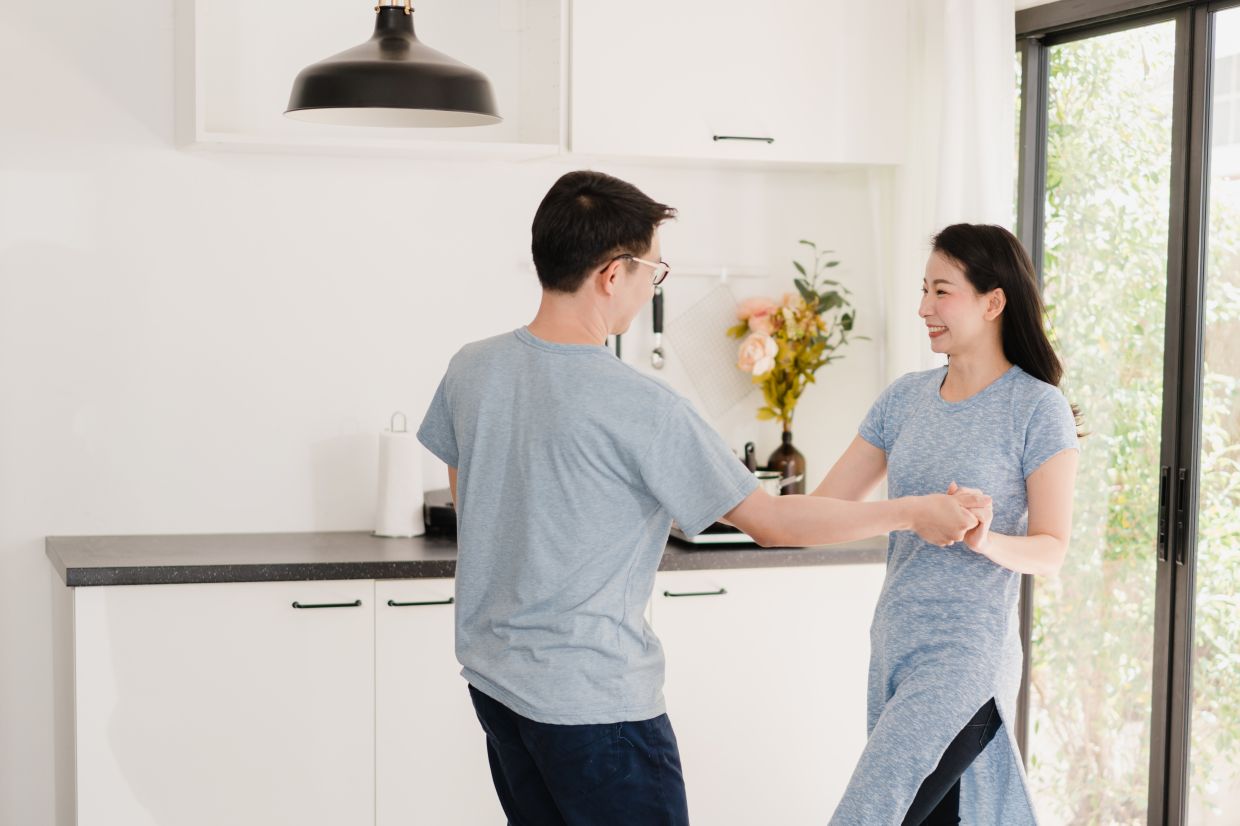 Young Asian couple listen to music and dancing after having breakfast at home. Attractive Japanese woman and handsome man are enjoying spending time together in modern kitchen at house in the morning.