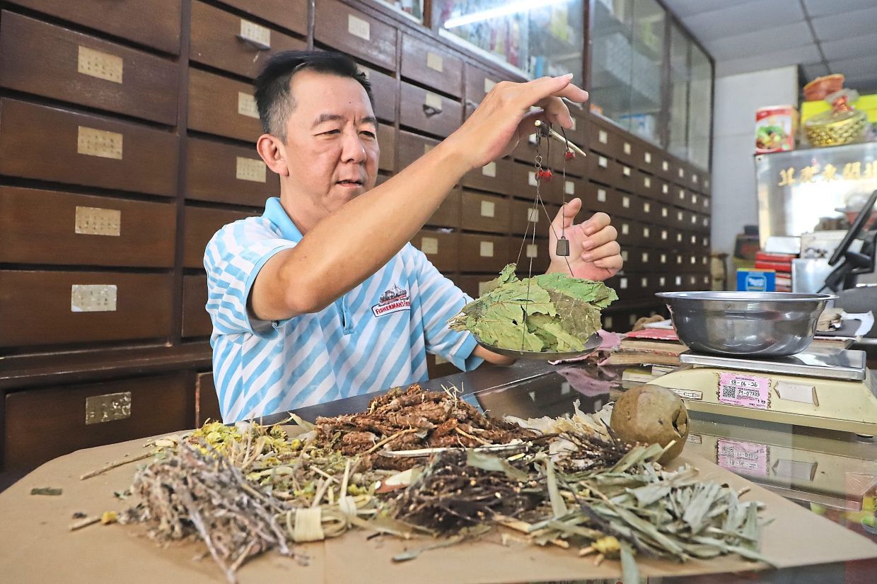 Cheong Hai Seng who specialises in traditional Chinese herbs and medicine weighing the herbs he puts together to make a concoction to cool the body down during the hot spell, at his shop along Jalan Perak, in George Town, Penang.( July 23, 2025 ) — LIM BENG TATT/The Star