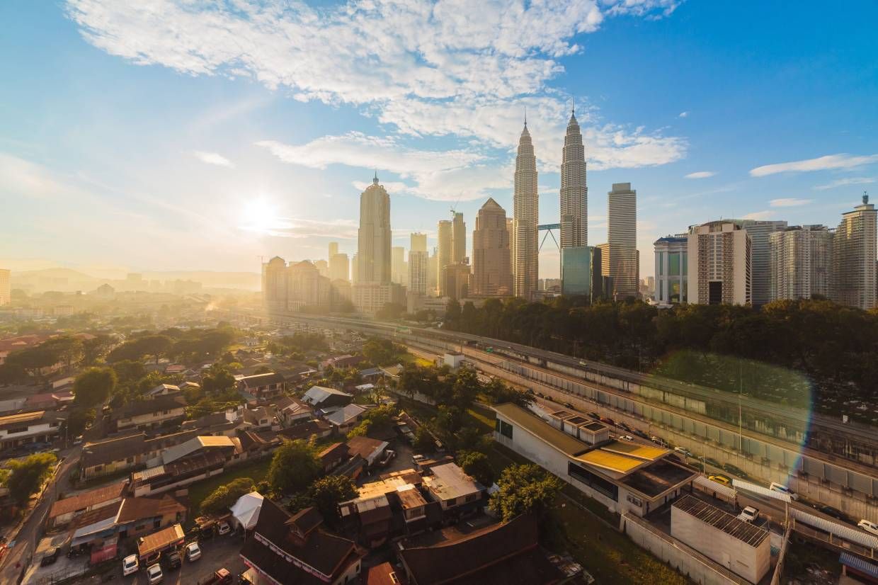 High vantage view of center of Kuala Lumpur during a clear sunrise with blinding sun and blue sky.