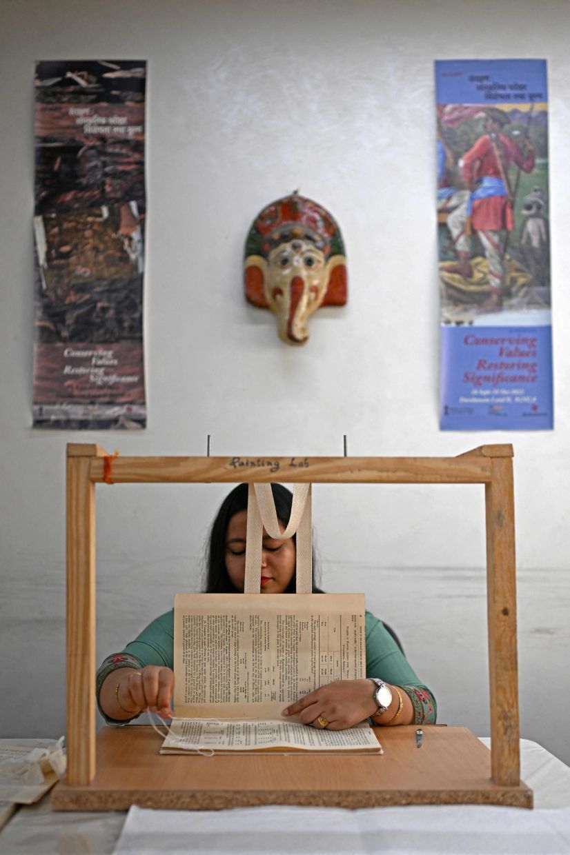 This photograph taken on June 23, 2025 shows an employee sewing a book inside the paper conservation lab of the conservation department at the Indira Gandhi National Centre for Arts (IGNCA), in New Delhi. In a climate-controlled room in India's capital, restorers carefully piece together rare historical documents and artefacts to rescue irreplaceable fragments that provide a unique window into New Delhi's past. Experts at the Indira Gandhi National Centre for the Arts (IGNCA) painstakingly revive crumbling maps and photographs that help track the development of the sprawling megacity now home to more than 30 million people. (Photo by Money SHARMA / AFP)