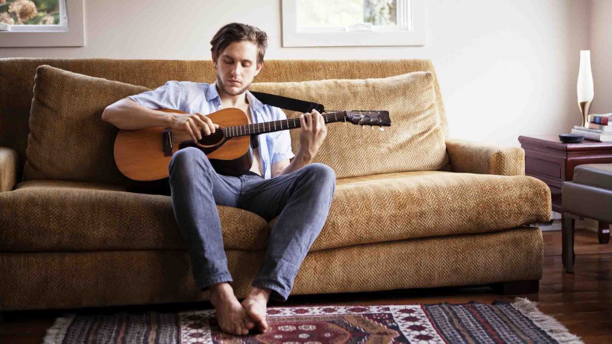 22 Dec 2011 --- Young man playing acoustic guitar on couch --- Image byCI2/Corbis