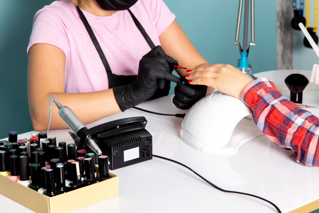 a front view young female manicure in pink t-shirt with black gloves and black mask doing manicure on the blue background manicurist nails beauty