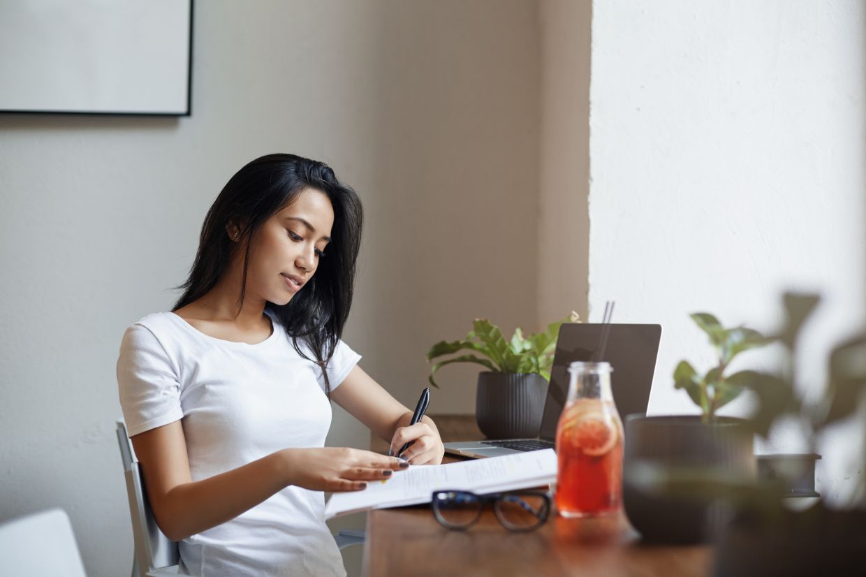 Beautiful left-handed girl studying in cafe, taking down notes in notebook, solving exercise near laptop, female entrepreneur plan schedule as drink juice and enjoy co-working space atmosphere.
