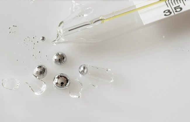 Broken glass mercury thermometer on light grey surface. Mercury drops with glass fragments. Mercury vapor poisoning.