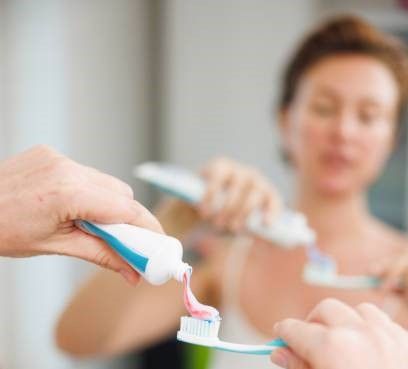 Woman doing her dental care routine in the morning, squeezing toothpaste on toothbrush in front of the bathroom mirror