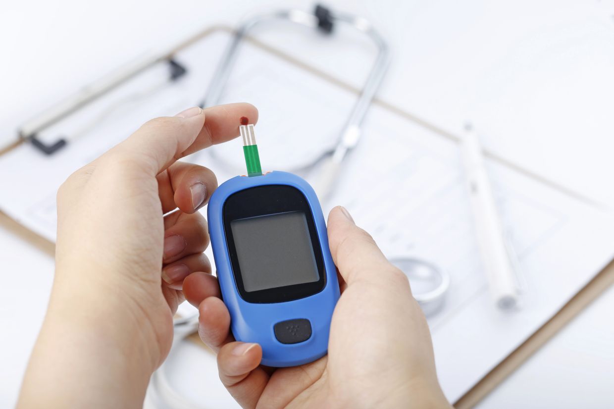 Hand holding a blood glucose meter measuring blood sugar, the background is a stethoscope and chart file