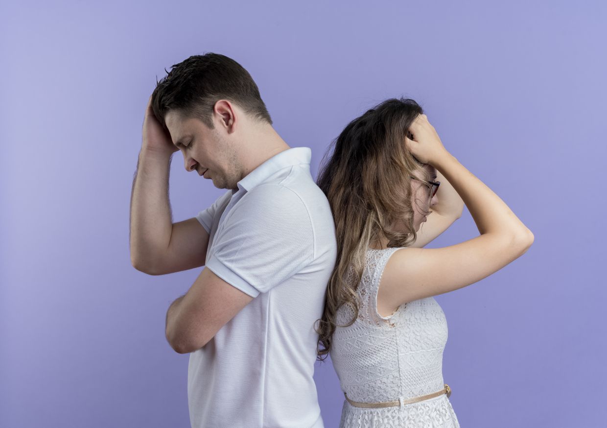 upset young couple man and woman standing back to back over blue background
