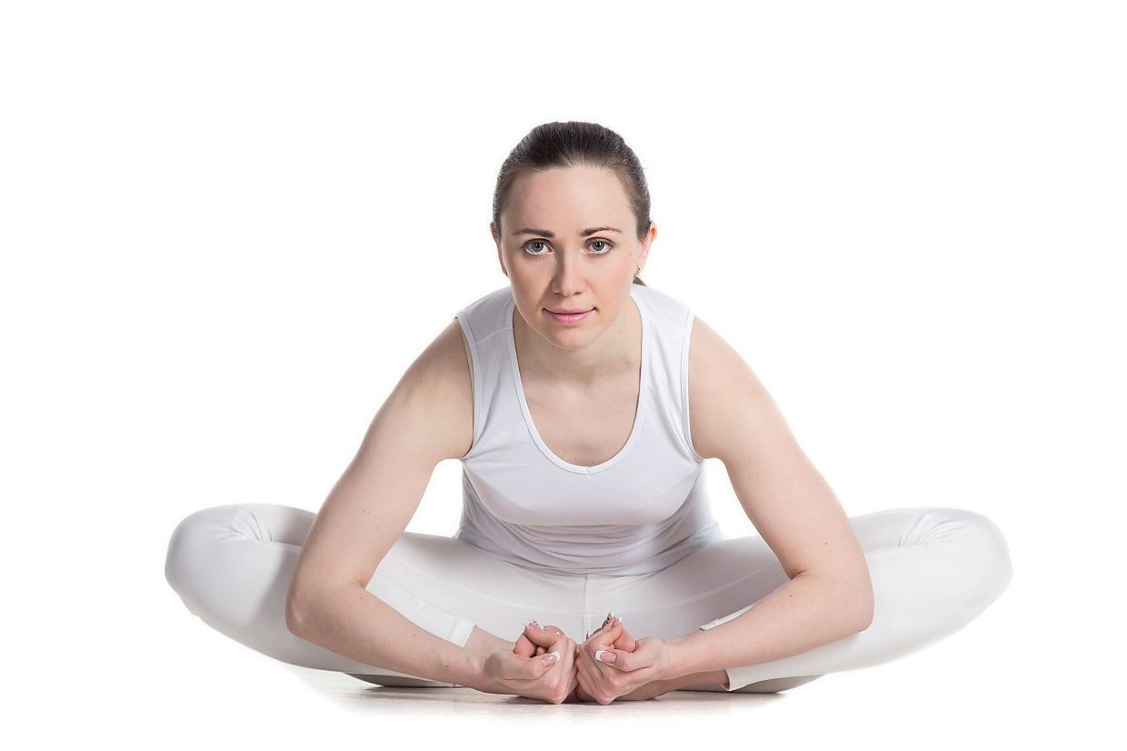 Sporty beautiful smiling young woman in white sportswear sitting in purna titli, Baddha Kona asana, bound angle, cobbler, butterfly pose, studio full length isolated shot, front view