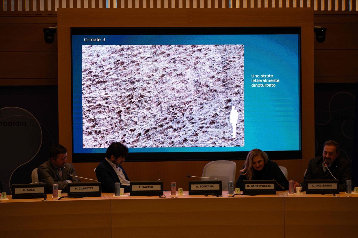 Paleontologist at the Natural History Museum of Milan Cristiano Dal Sasso (R) commentsphotos on a screen during a press conference to present the discovery of thousands of dinosaur tracks discovered in Italy's Stelvio National Park near the areas that will host the Milano-Cortina 2026 Olympic Games, in Milan on December 16, 2025. The tracks are estimated to belong to Late Triassic prosauropod dinosaurs, dating back 210 million years. (Photo by Piero CRUCIATTI / AFP)