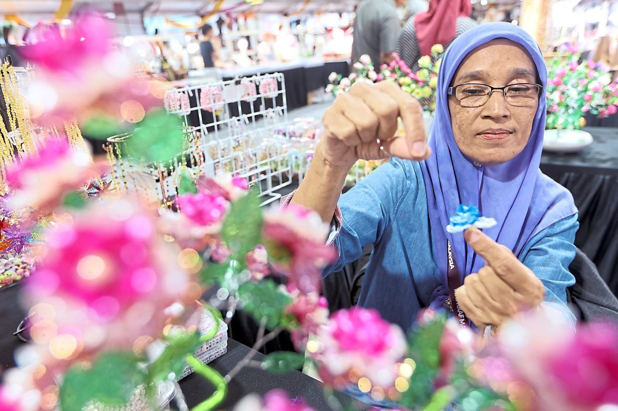 Crystal beading artisan Rosnah Bakar arranging a flower made of crystal and acrylic, twisting fine wire to secure each piece. — THOMAS YONG/The Star