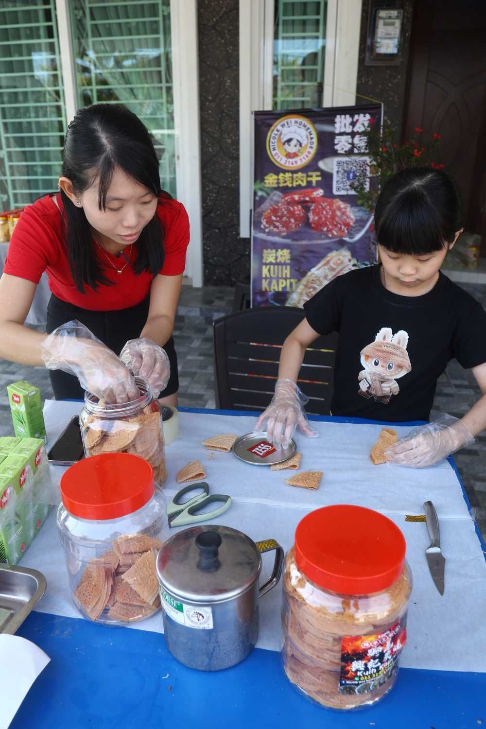 Nicole Wei,35,(in red) and nine-year-old daughter Kwong Zhi Qi helps out at their house in making home-made kuih kapit in Kampung Simee.-(25th January 2025)-RONNIE CHIN/The Star