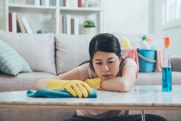 asian wife resting her head and arms on table in living room wants to take a nap. beautiful housewife doing housework in house. young lady feeling tired wiping table in the afternoon.